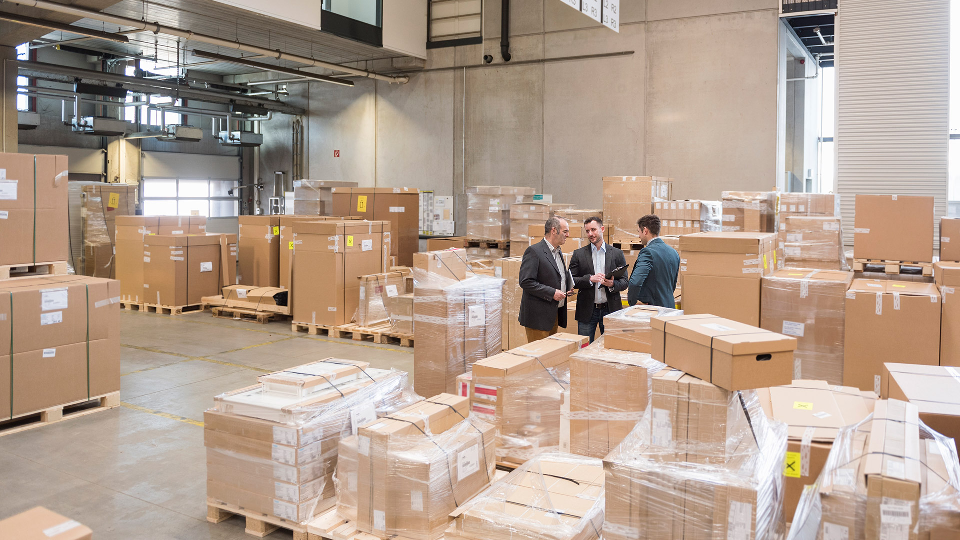 Mężczyźni rozmawiający na magazynie wypełnionym kartonami.