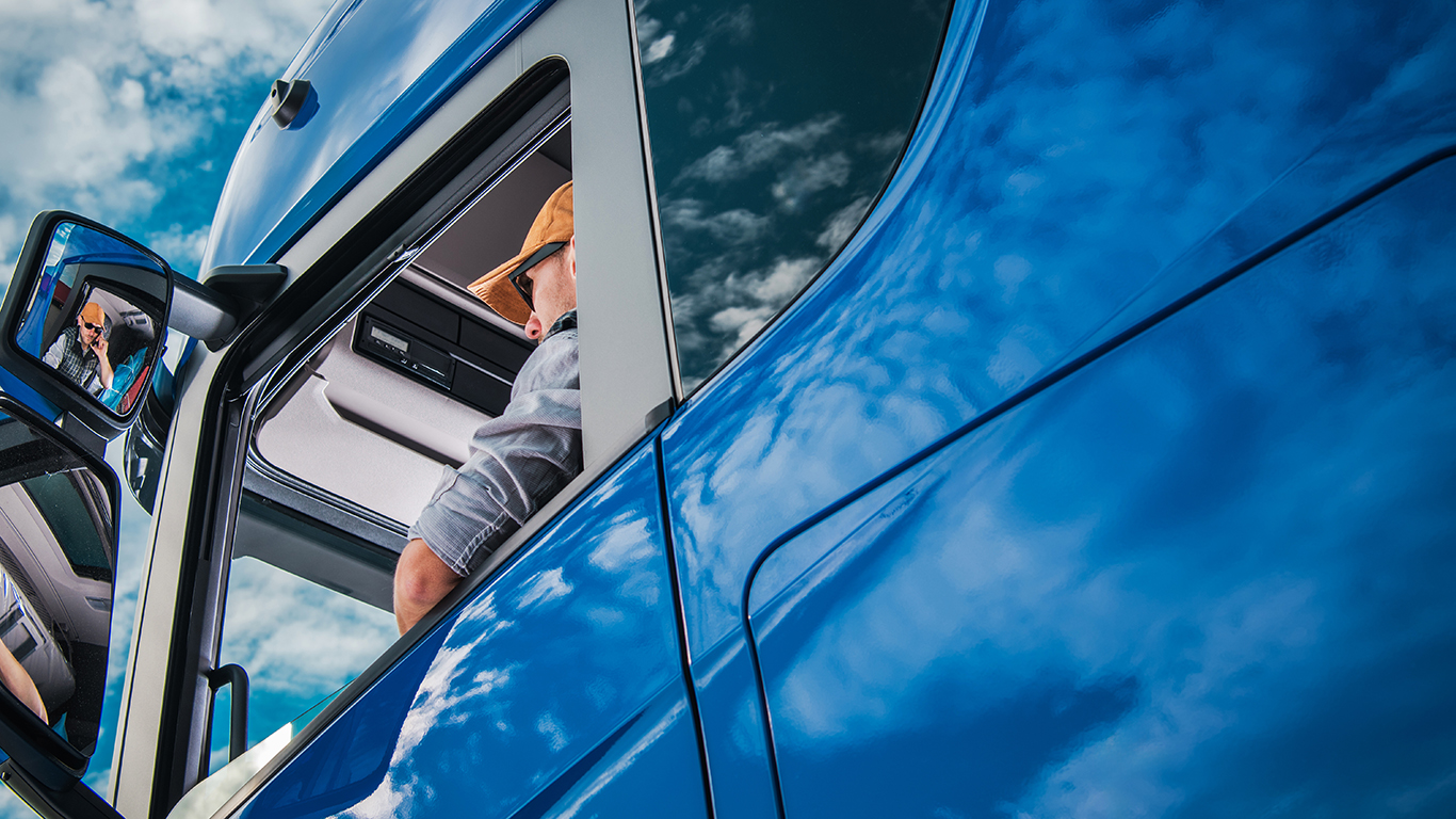 Kierowca ciężarówki siedzący na fotelu w niebieskiej ciężarówce z naczepą.