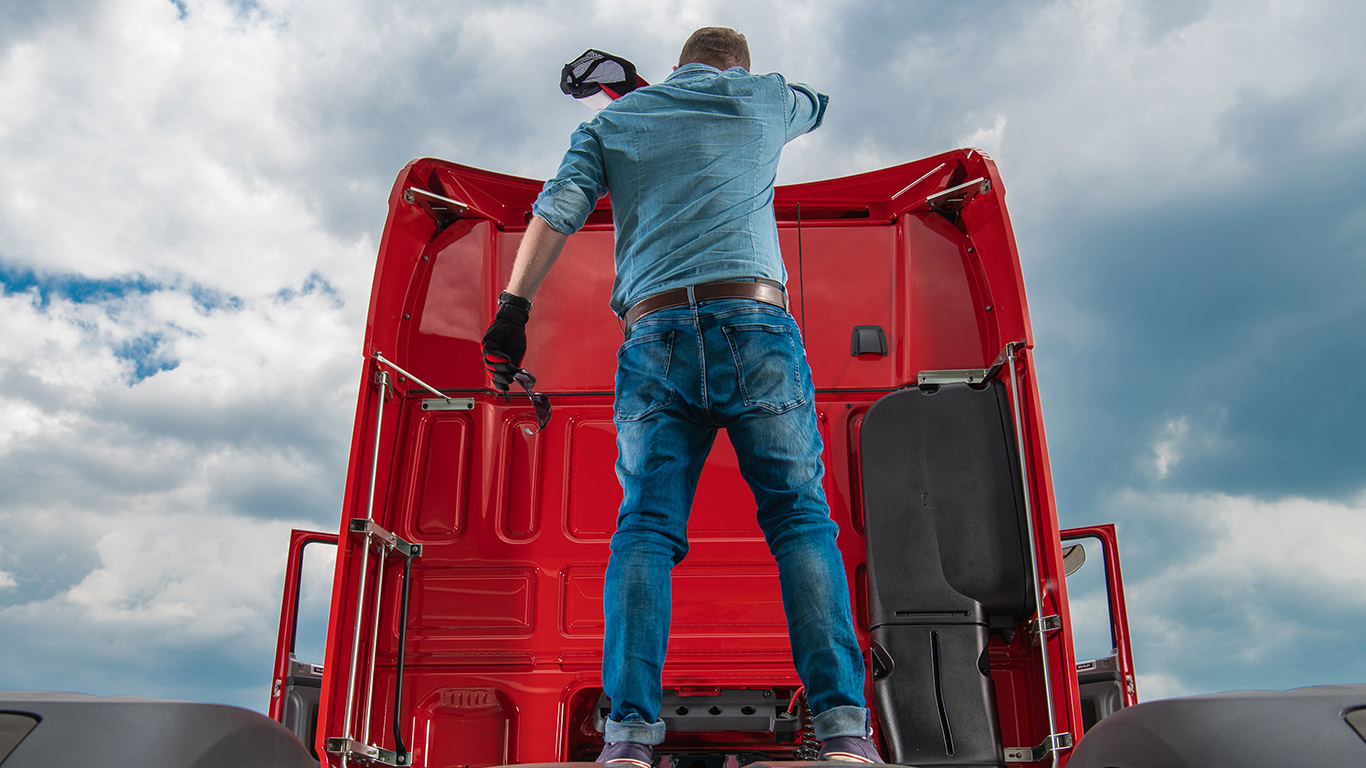 Mężczyzna z czapką w ręce stojący na ciągniku siodłowym.