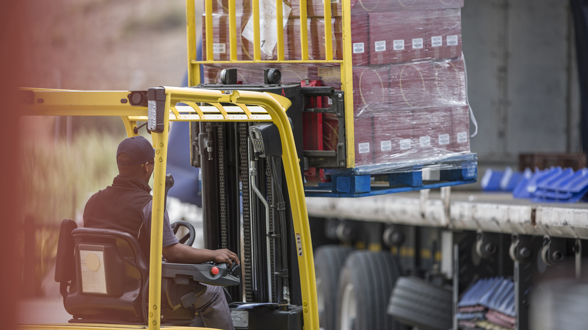 Meżczyzna w wózku widłowym prowadzący załadunek towaru na naczepę.