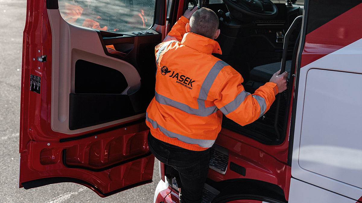 Mężczyzna w kamizelce odblaskowej wchodzący do ciągnika siodłowego.